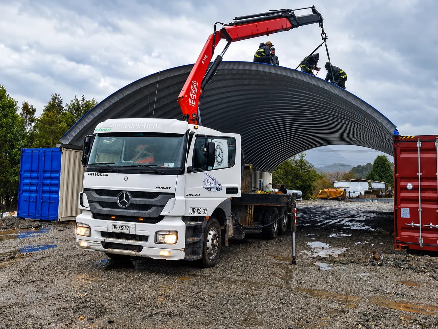 Camión grúa Mercedes-Benz Axor con pluma Fassi F175 izando la techumbre curva de un galpón